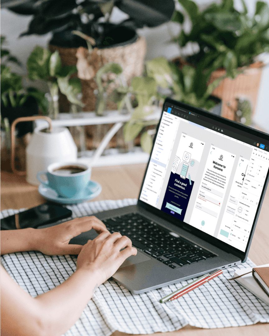 Person working on a laptop displaying web design templates, with coffee and plants on a desk in a home office workspace