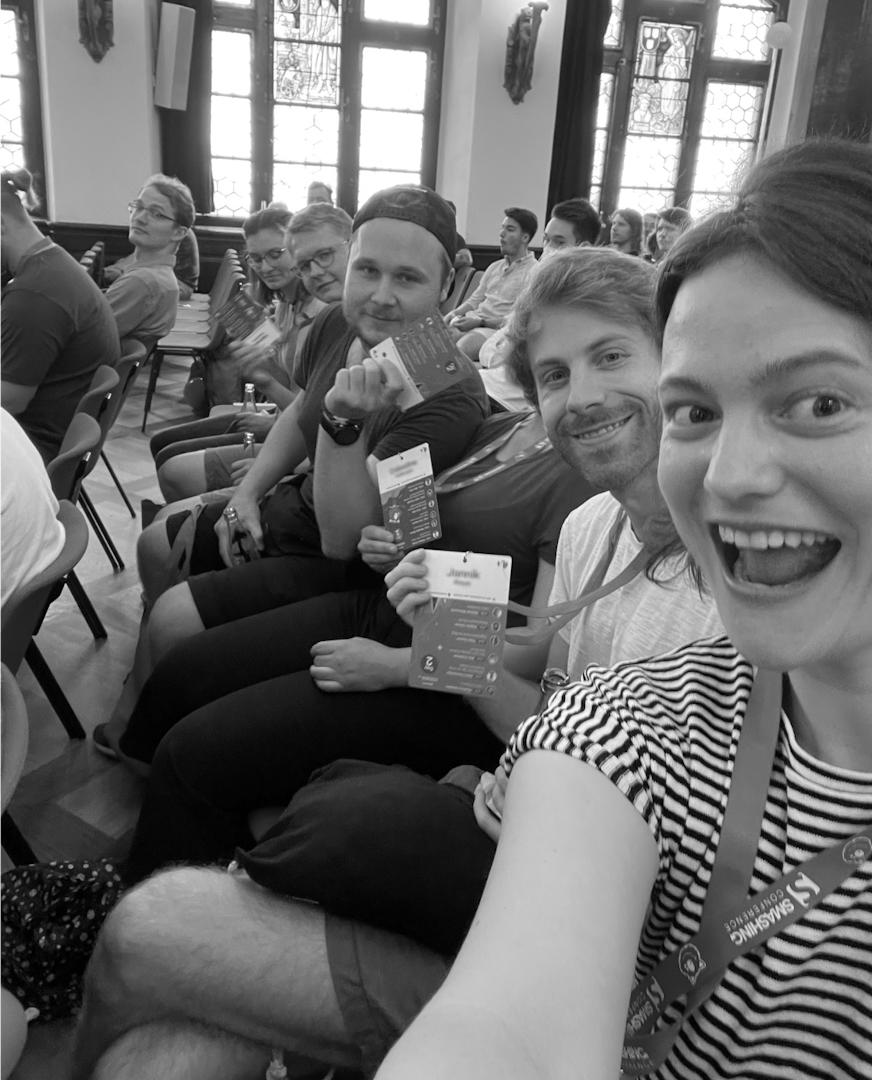 Group of conference attendees sitting together holding materials and smiling at the camera in a cheerful event setting
