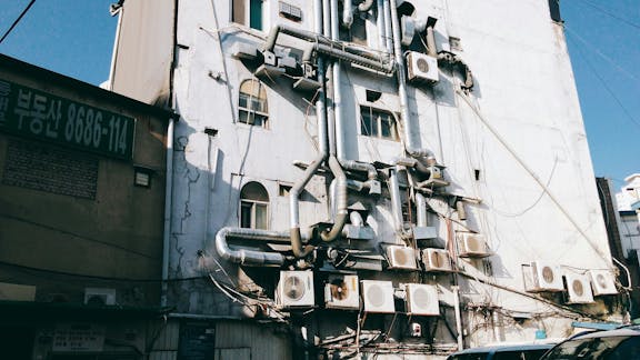 Deteriorating facade of a multi-story residential building covered with numerous air conditioning units and electrical wiring