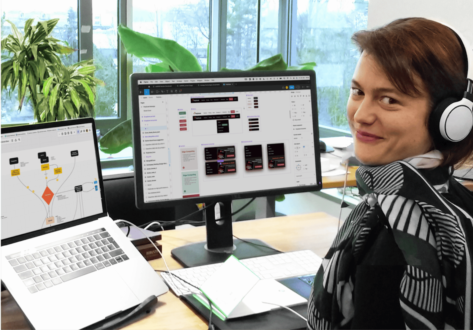 Frau mit Kopfhörern arbeitet an ihrem Arbeitsplatz mit mehreren Bildschirmen und zeigt eine Design-Software mit UI-Elementen und Grafiken.
