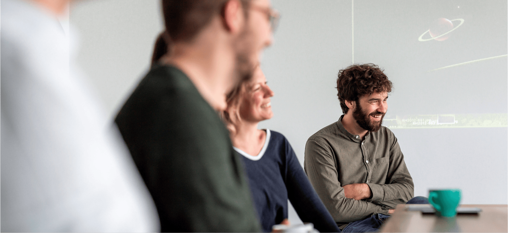 Three people in a seminar room, one speaking in front of a presentation on the whiteboard.