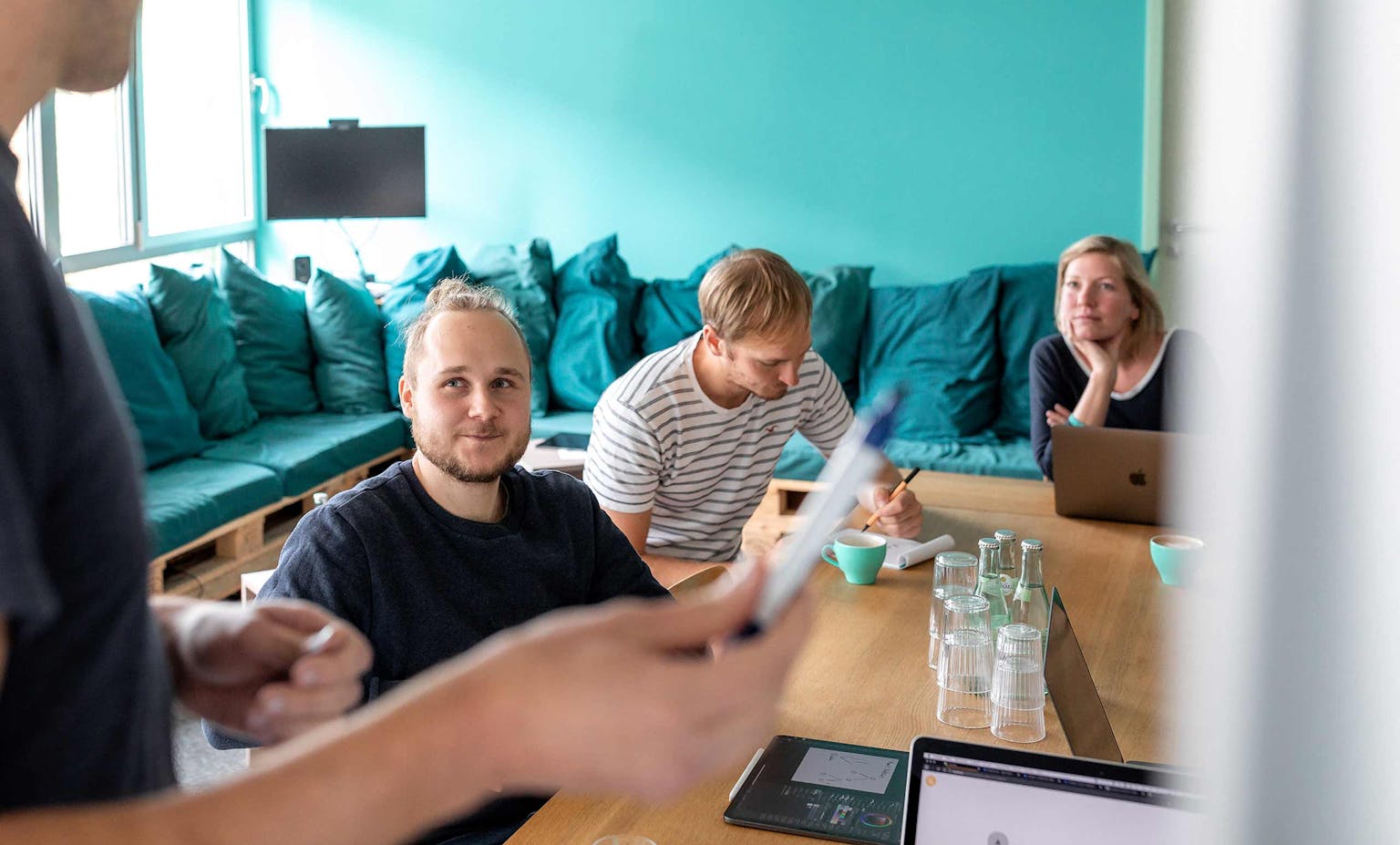 Team meeting at Peerigon office Team members in a meeting in a modern office with turquoise wall and cushioned seating