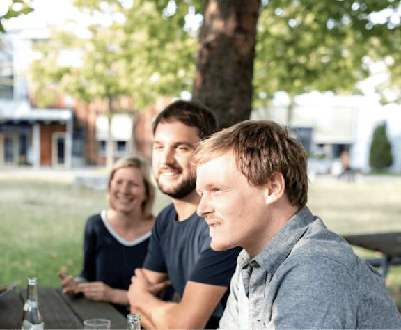 Collegial Meeting Outdoors Three Peeris sitting together at an outdoor table under a tree