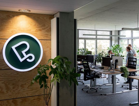 Peerigon Office and Workspace Peerigon office interior with illuminated green logo on wooden wall, desks with computers, and employees working by windows