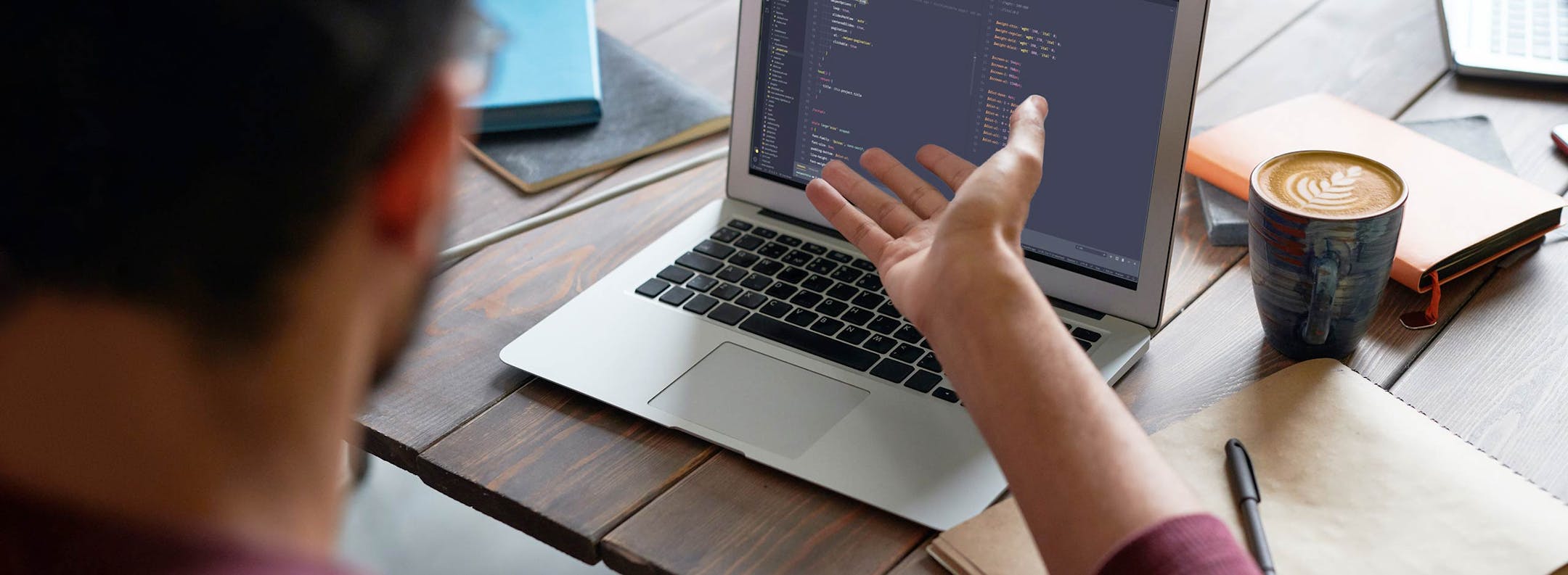 Software Development Workshop Developer working on code displayed on laptop screen during a workshop, with coffee and notebook on desk.