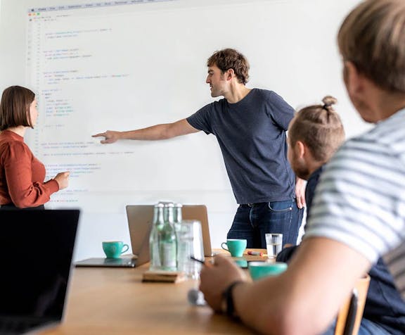 Softwareentwickler erklärt Code vor Whiteboard während Workshop mit Kollegen