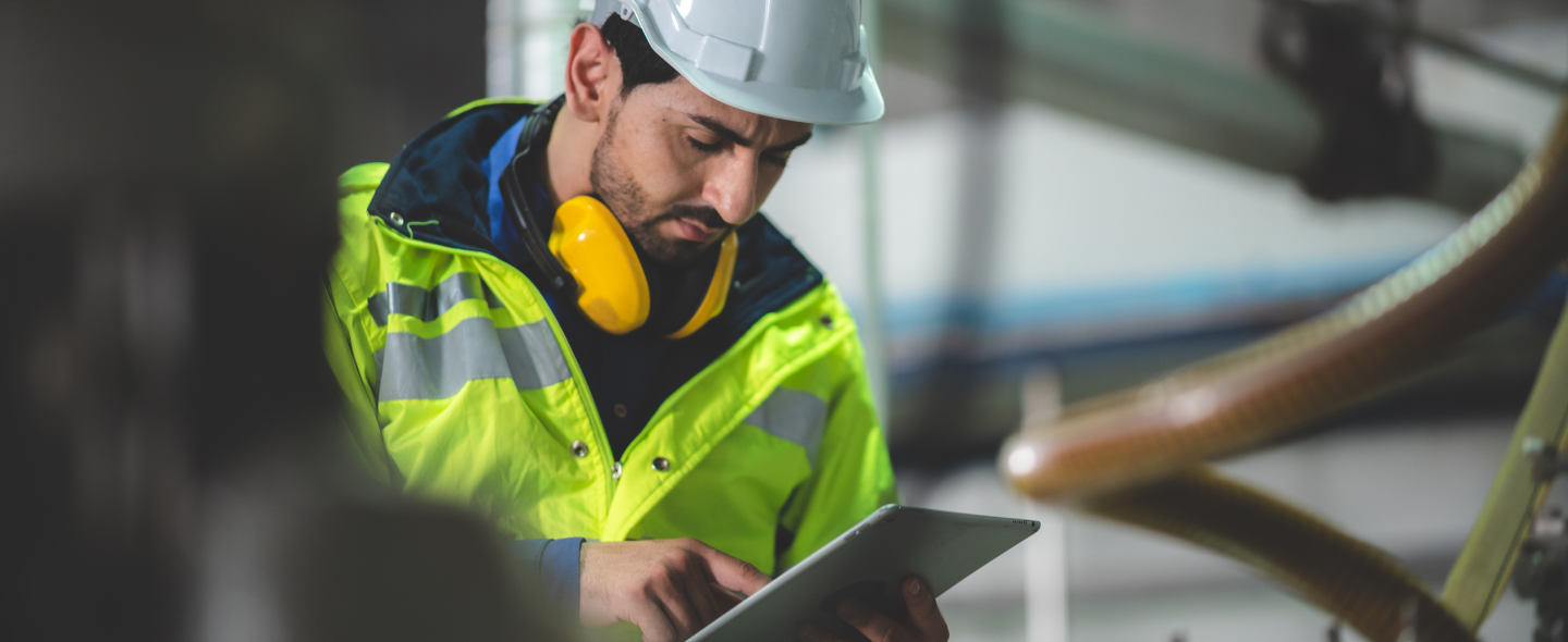 Factory worker scrutinizing tablet and clicking.