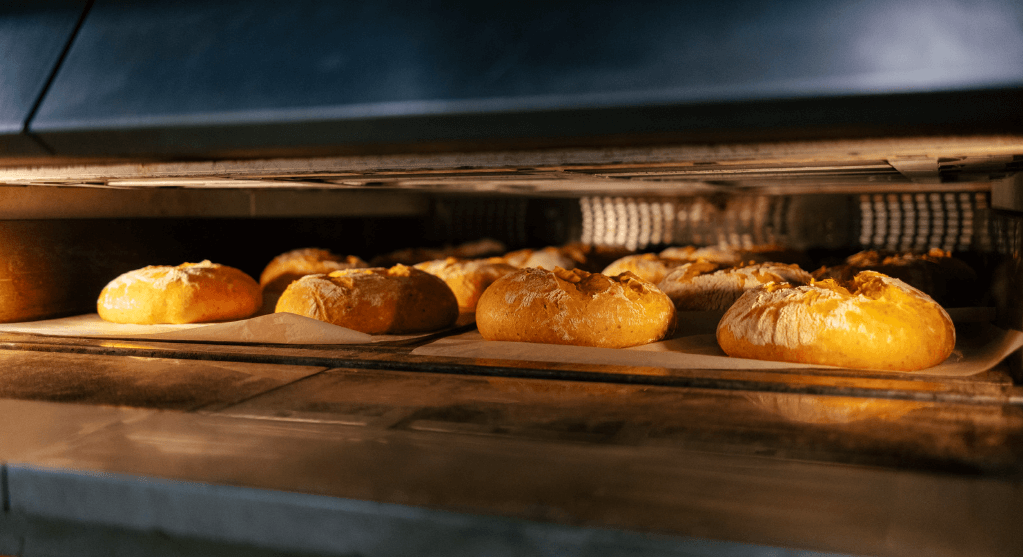 Golden brown rolls baking in an oven, placed on a parchment-lined tray.