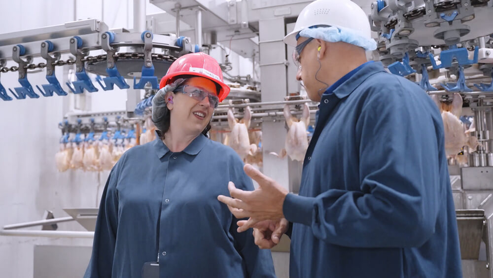 Executive smiling with protective hard hat while talking to production supervisor on the floor