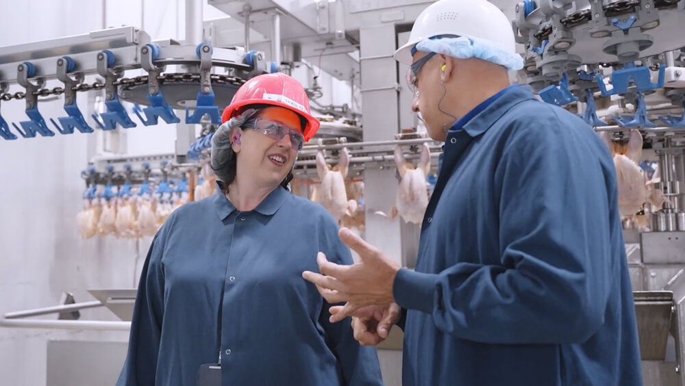Executive smiling with protective hard hat while talking to production supervisor on the floor