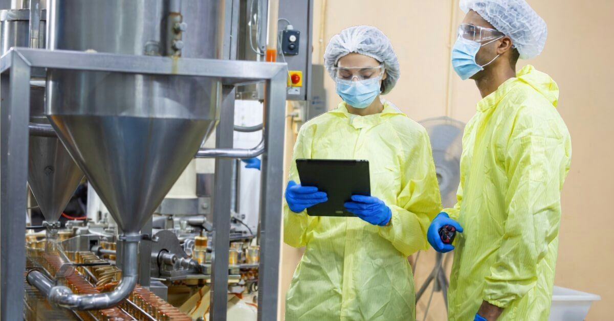 two food manufacturing workers in PPE checking line performance on a tablet