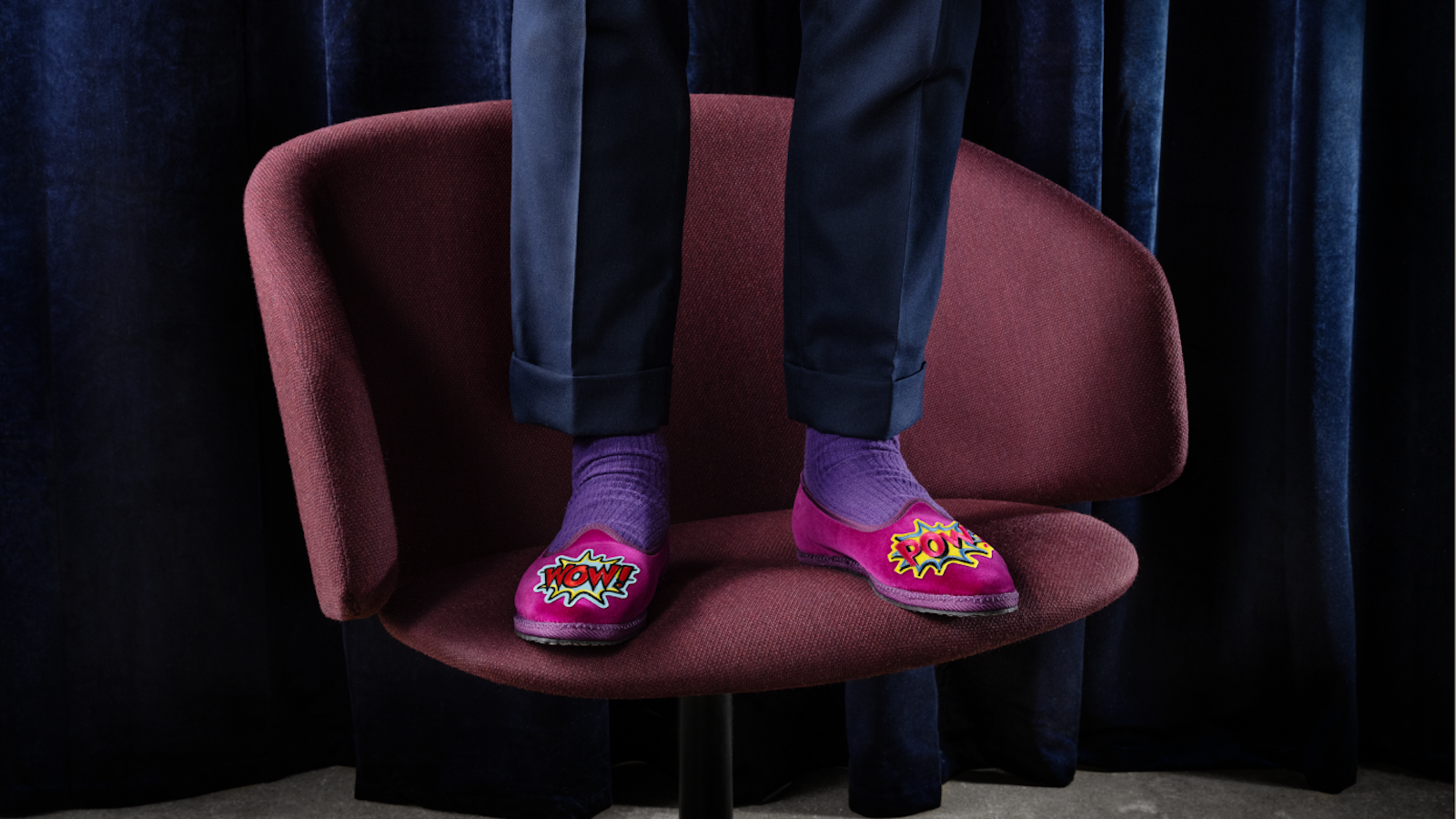 Cropped image showing only a person's legs and feet wearing pink slippers with the word 'POW' on them, standing on a chair.