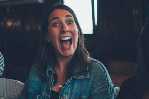 Woman with long brown hair smiling widely, wearing a denim jacket.