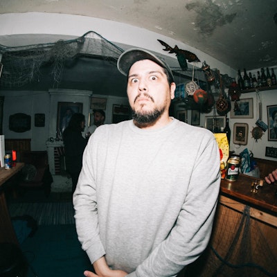 Man with a surprised expression in a dimly lit room decorated with various items.