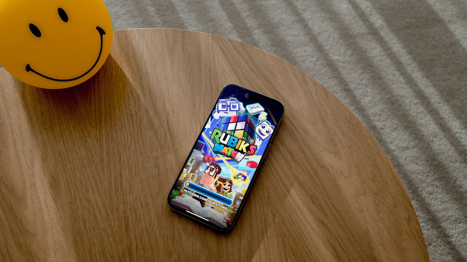 Smartphone displaying a Rubik's Cube game on a wooden table next to a smiling yellow lamp.