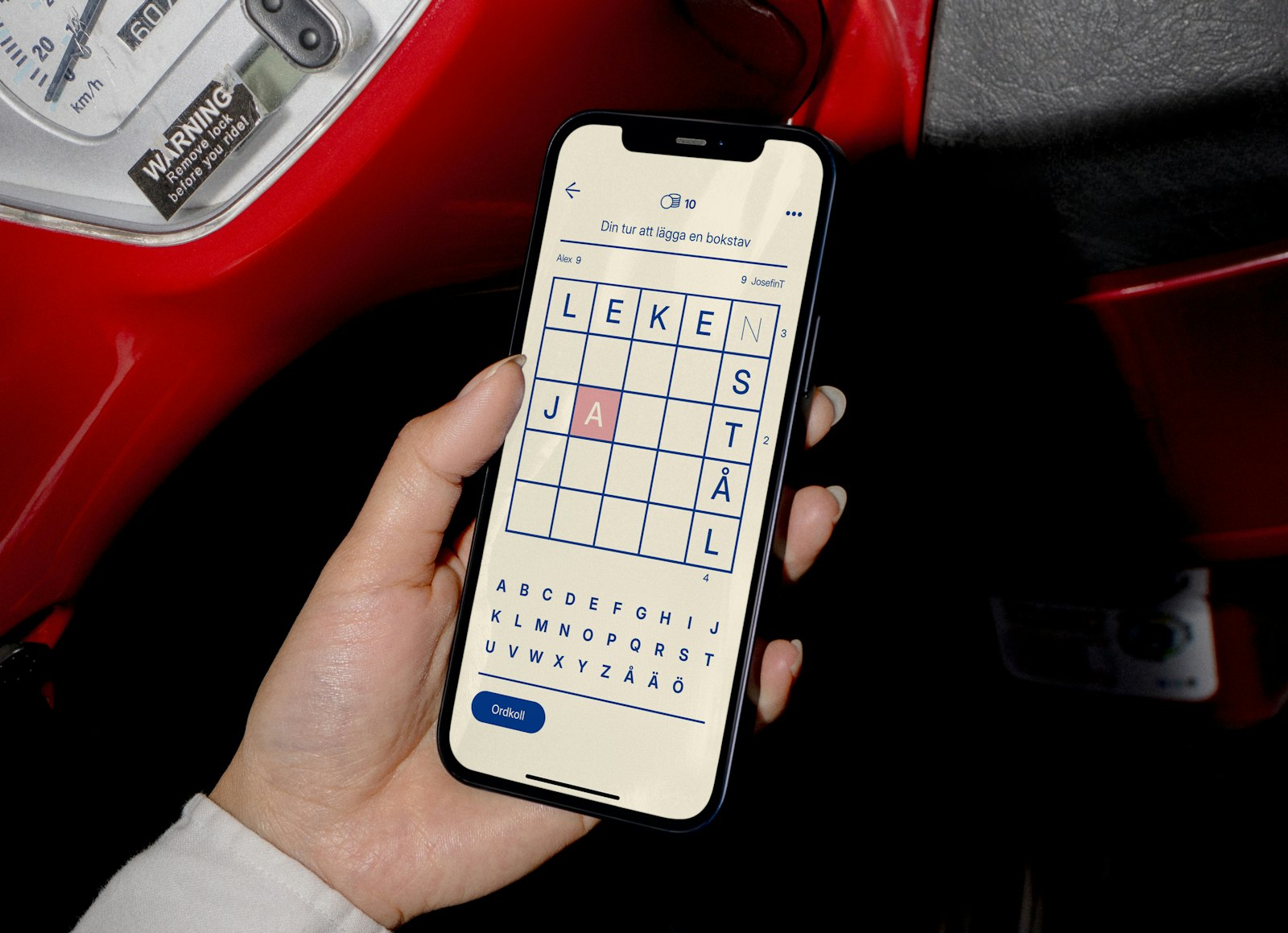 A hand holding a smartphone displaying a word puzzle game with a grid and letters.