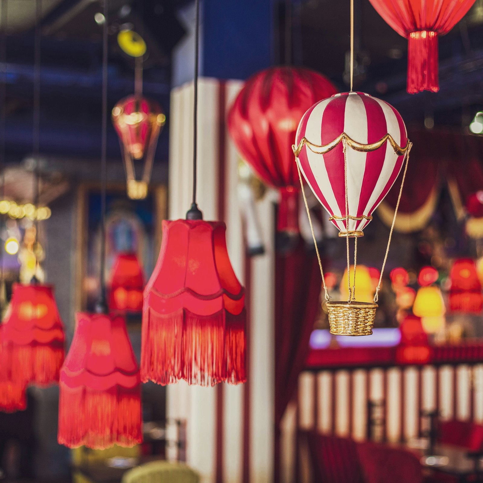Red and white hot air balloon light fixture among red fringe lamps in a colorful interior.