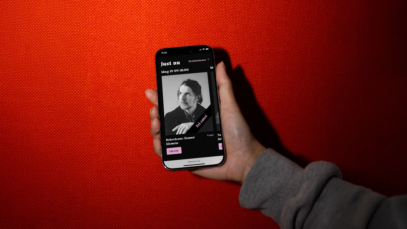 Hand holding a smartphone displaying a black and white portrait with event details on a red background.