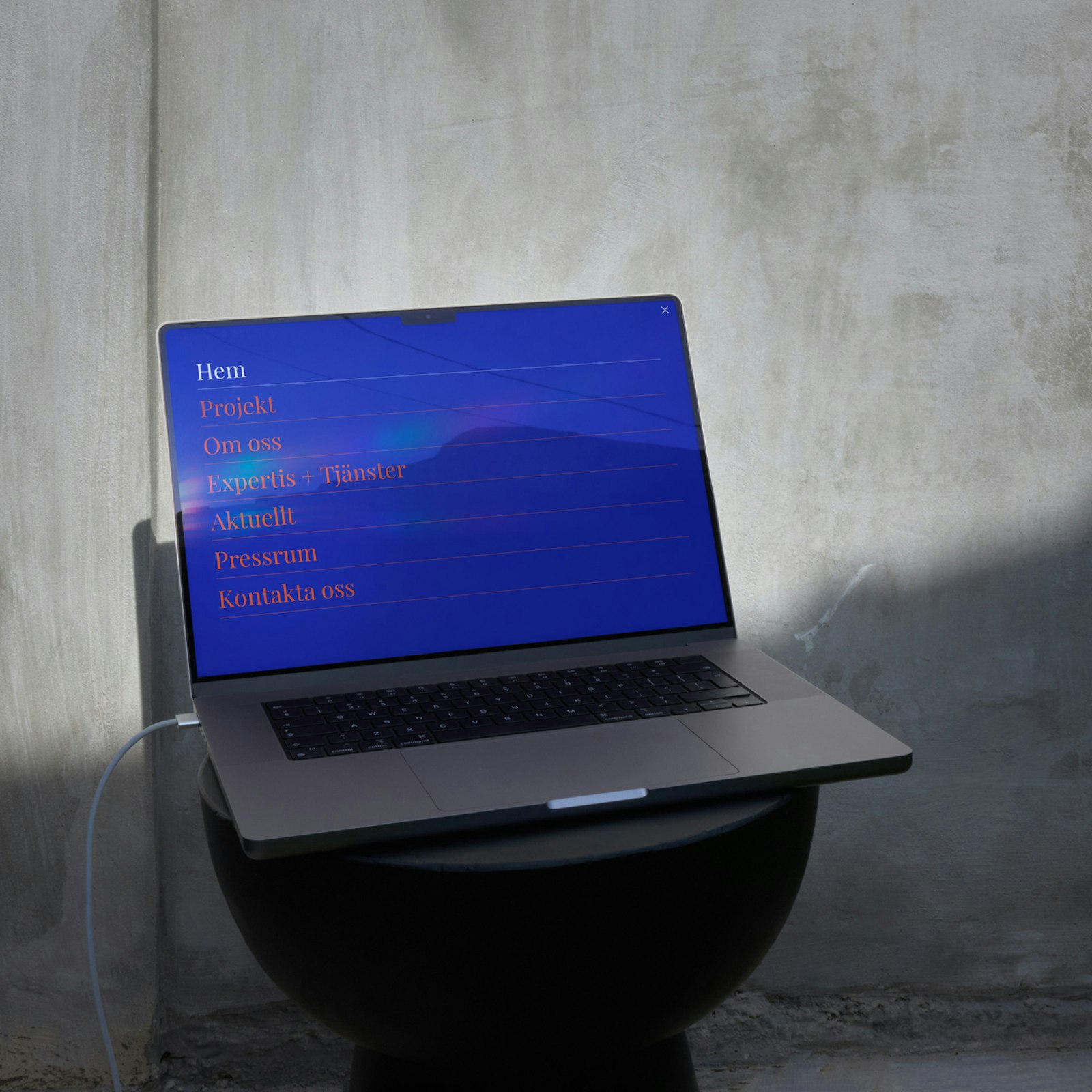 Laptop displaying a blue screen with menu options: Hem, Projekt, Om oss, Experter + Tjänster, Aktuellt, Pressrum, Kontakta...