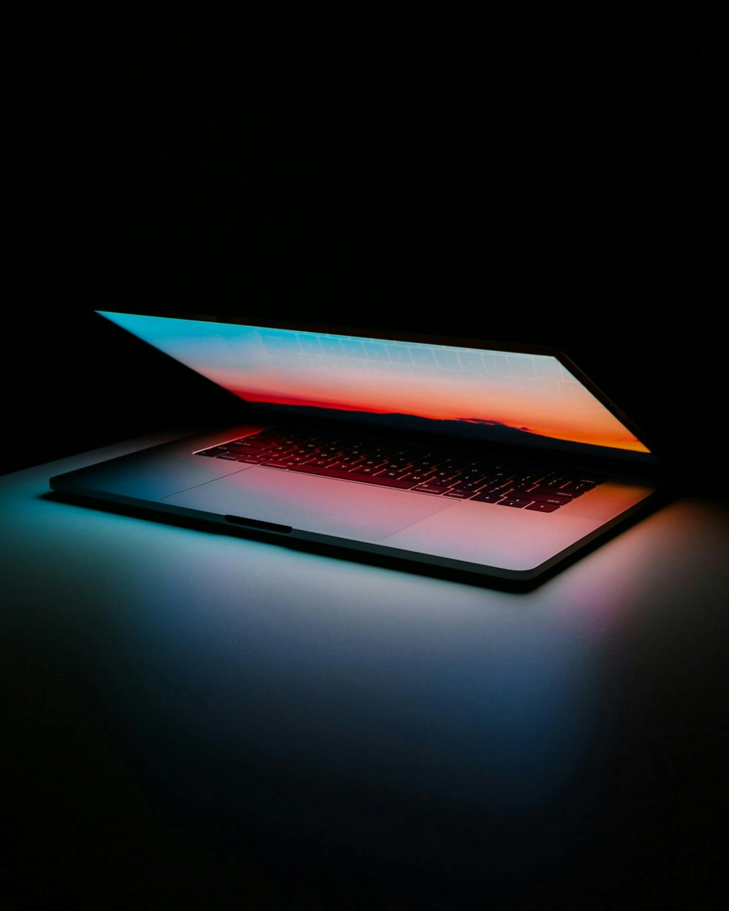 asdf A laptop with an illuminated keyboard and screen glowing in a dark room.