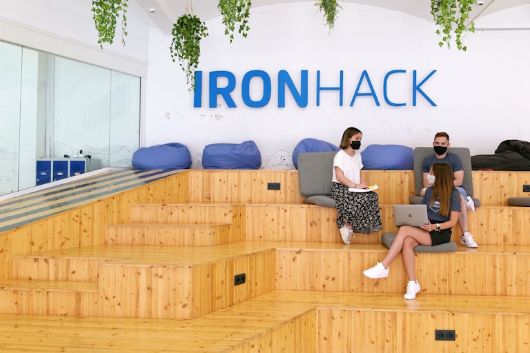 group of Ironhack students at campus with the logo behind them