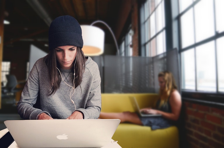 image of a tech girl working on her macbook and a colleague sit behind her