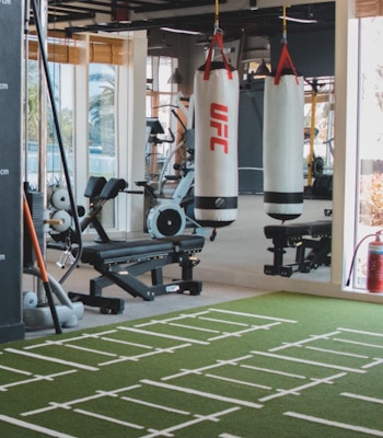 Optimal Fitness Interior view of a gym with exercise equipment, UFC punching bags, and a turf training area.