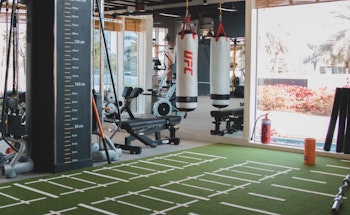Interior view of a gym with exercise equipment, UFC punching bags, and a turf training area.