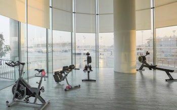 Gym area with stationary bikes, benches, and floor-to-ceiling windows providing ample natural light and cityscape views.