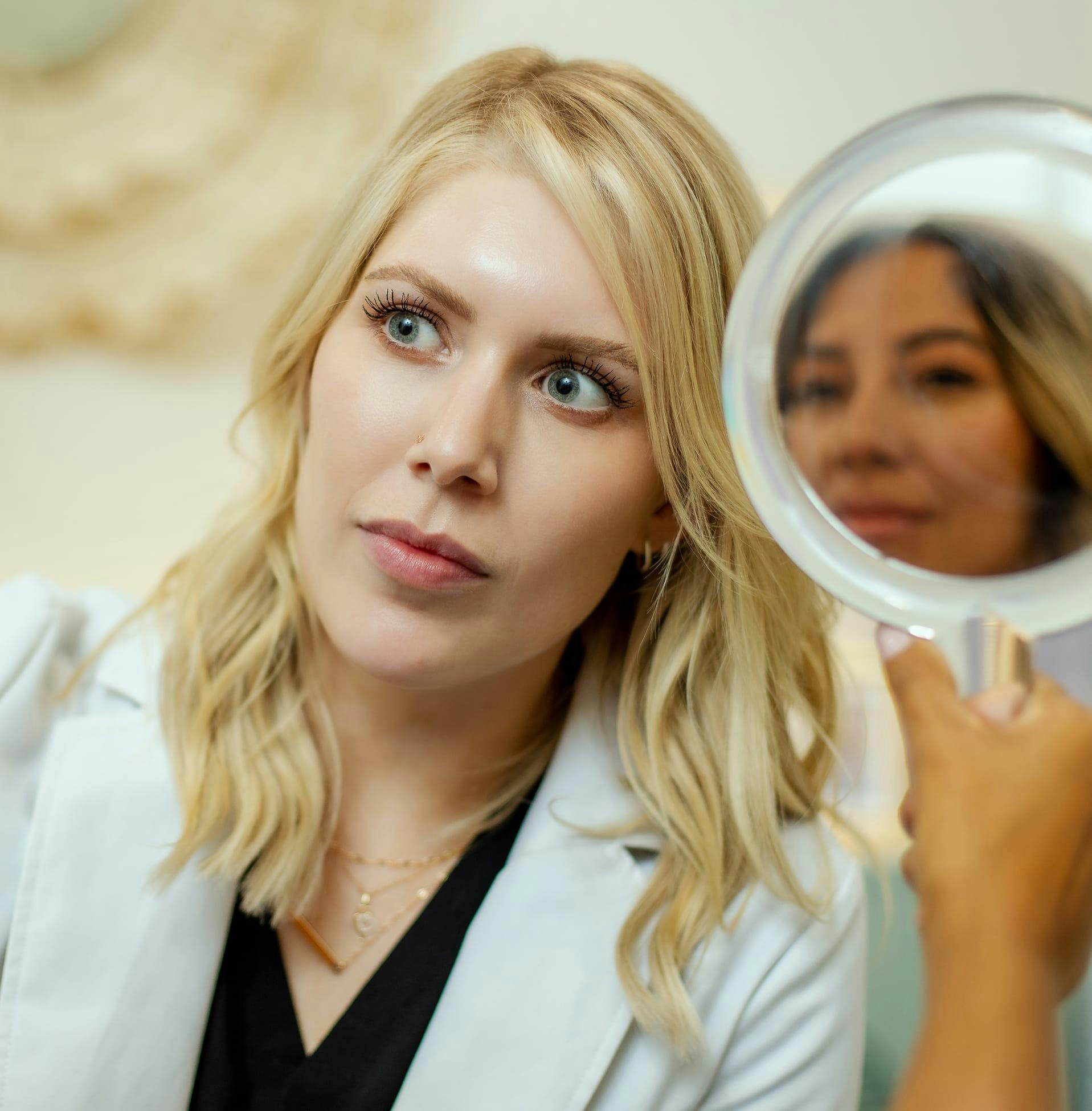 woman looking at another woman as she holds handheld mirror