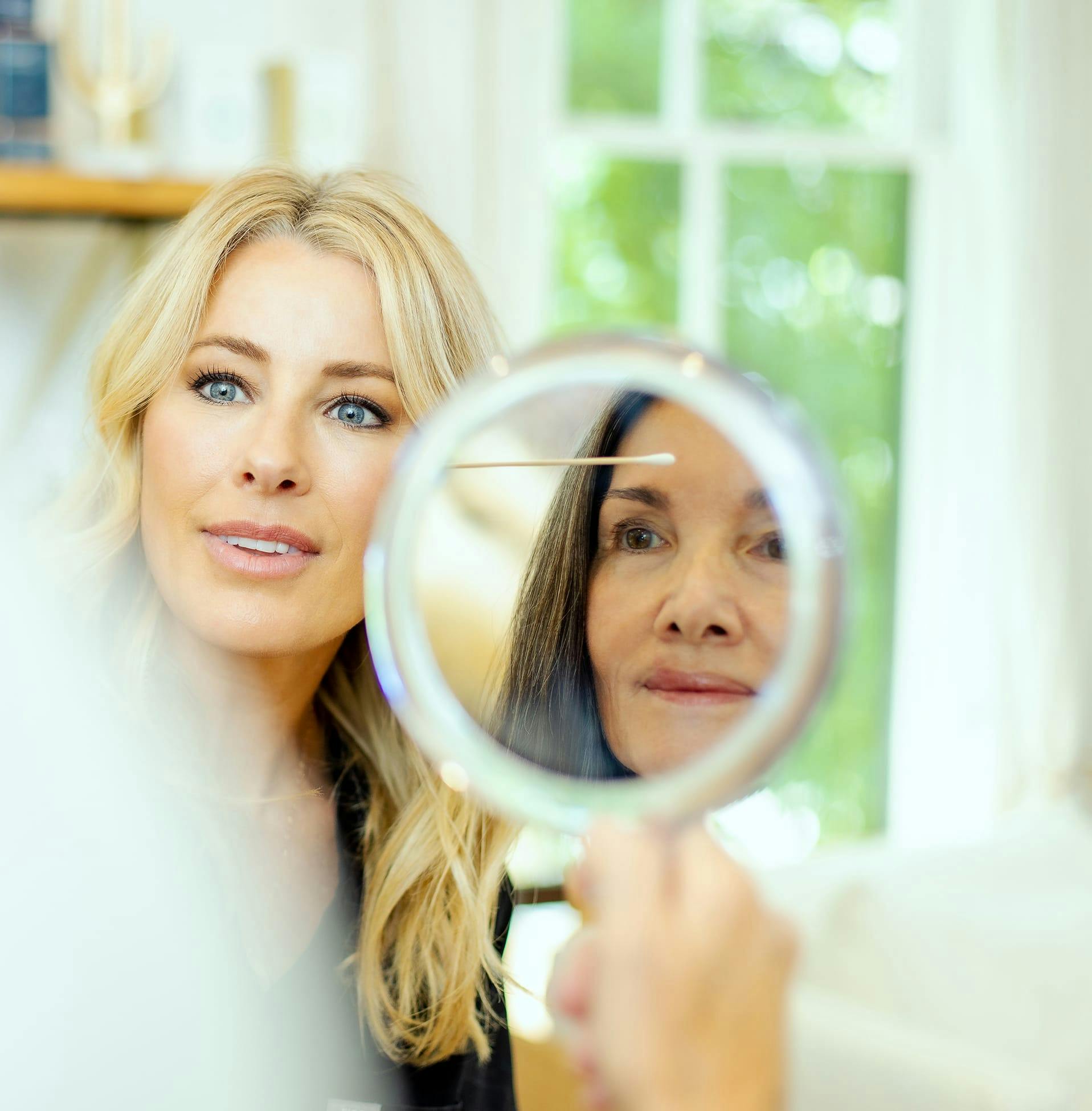 woman holding hand held while another woman looks at her forehead