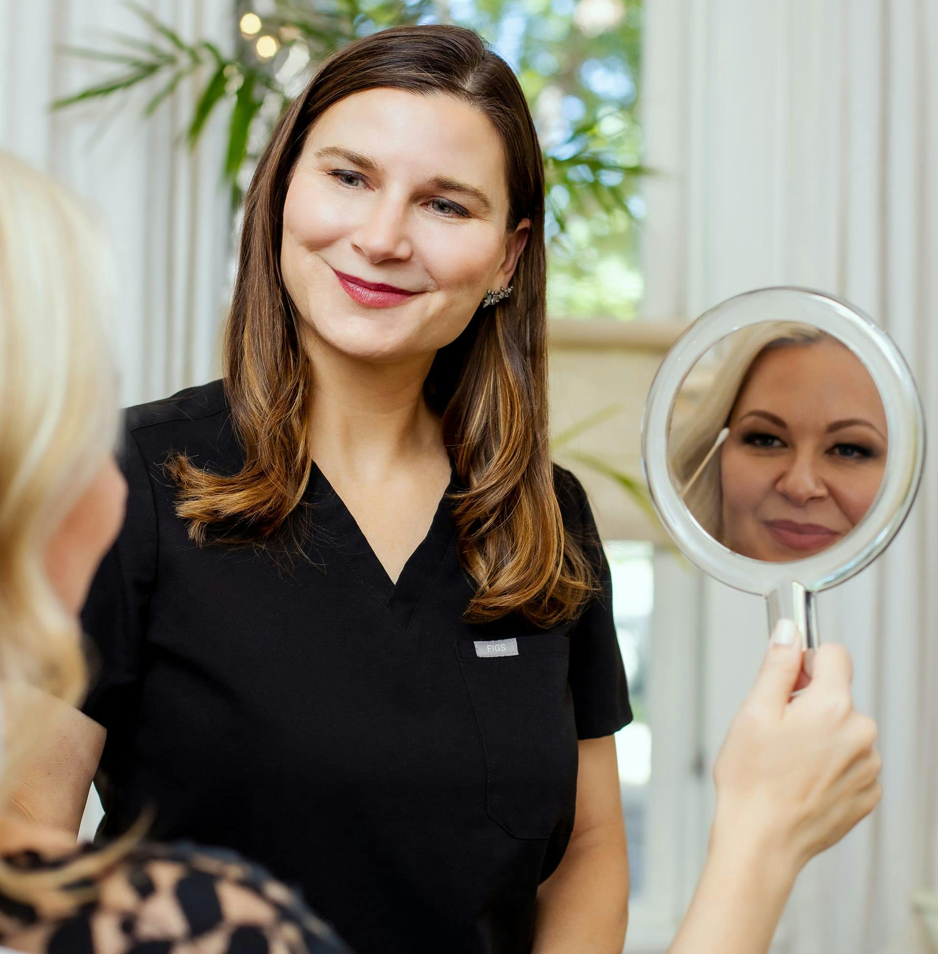 patient looking in handheld mirror with staff member examining her face