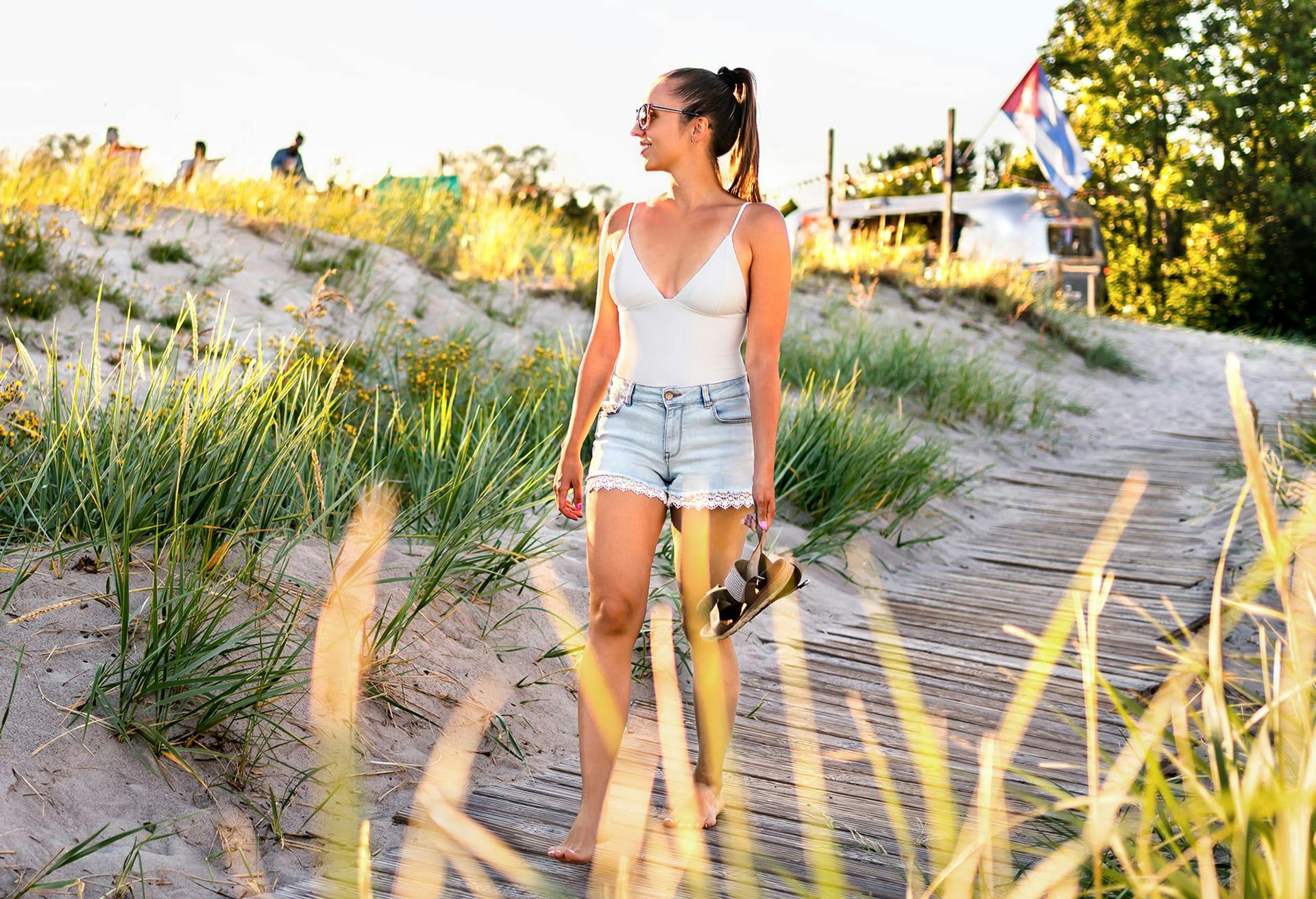 woman walking on board walk while holding her sandals