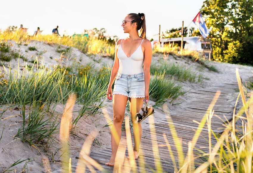 woman walking on board walk while holding her sandals