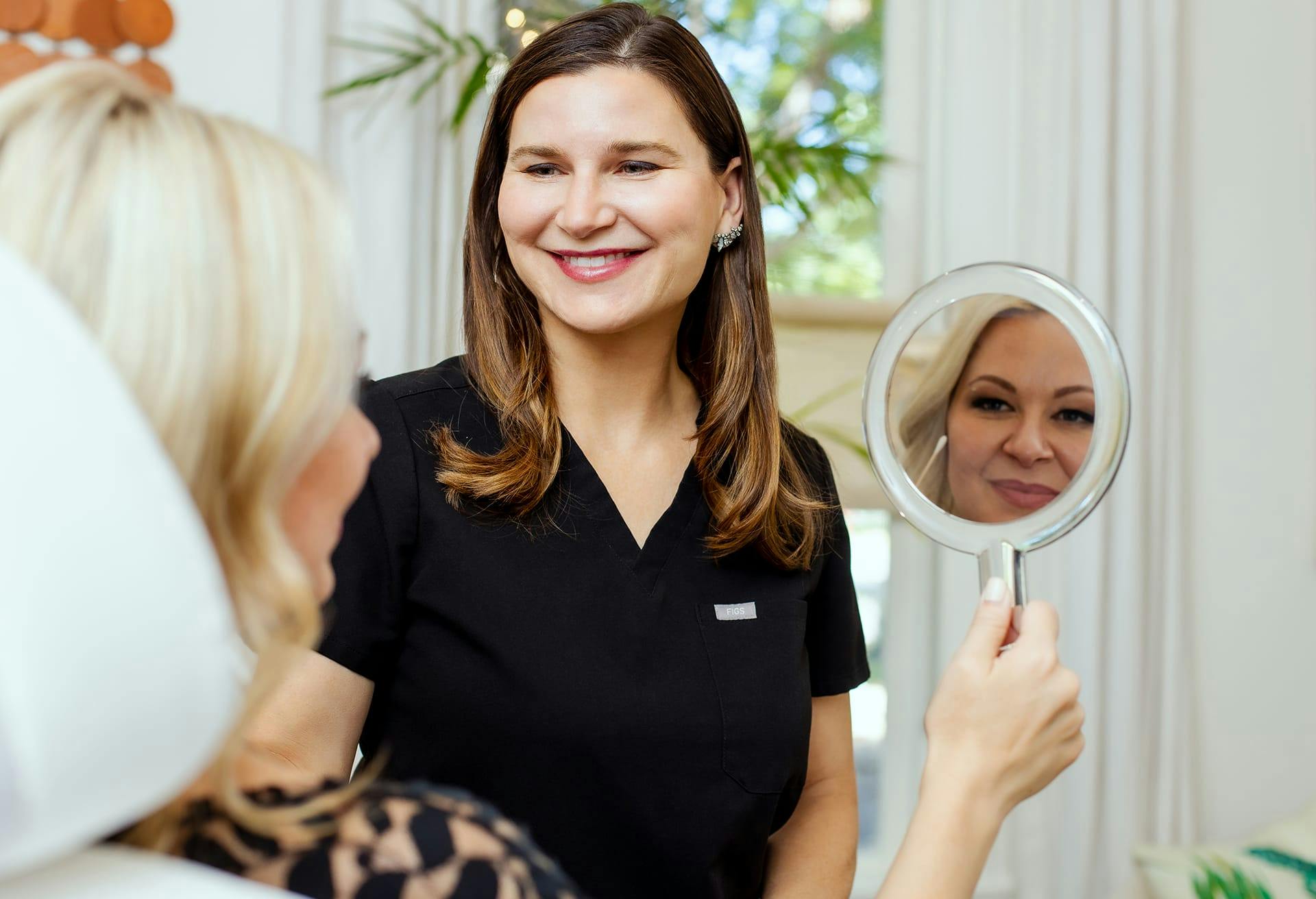 woman smiling at another woman while shes looking in handheld mirror