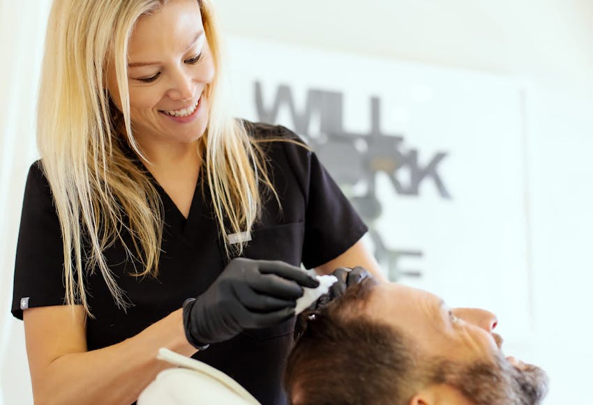 woman clipping mans hair back as he lays in exam chair