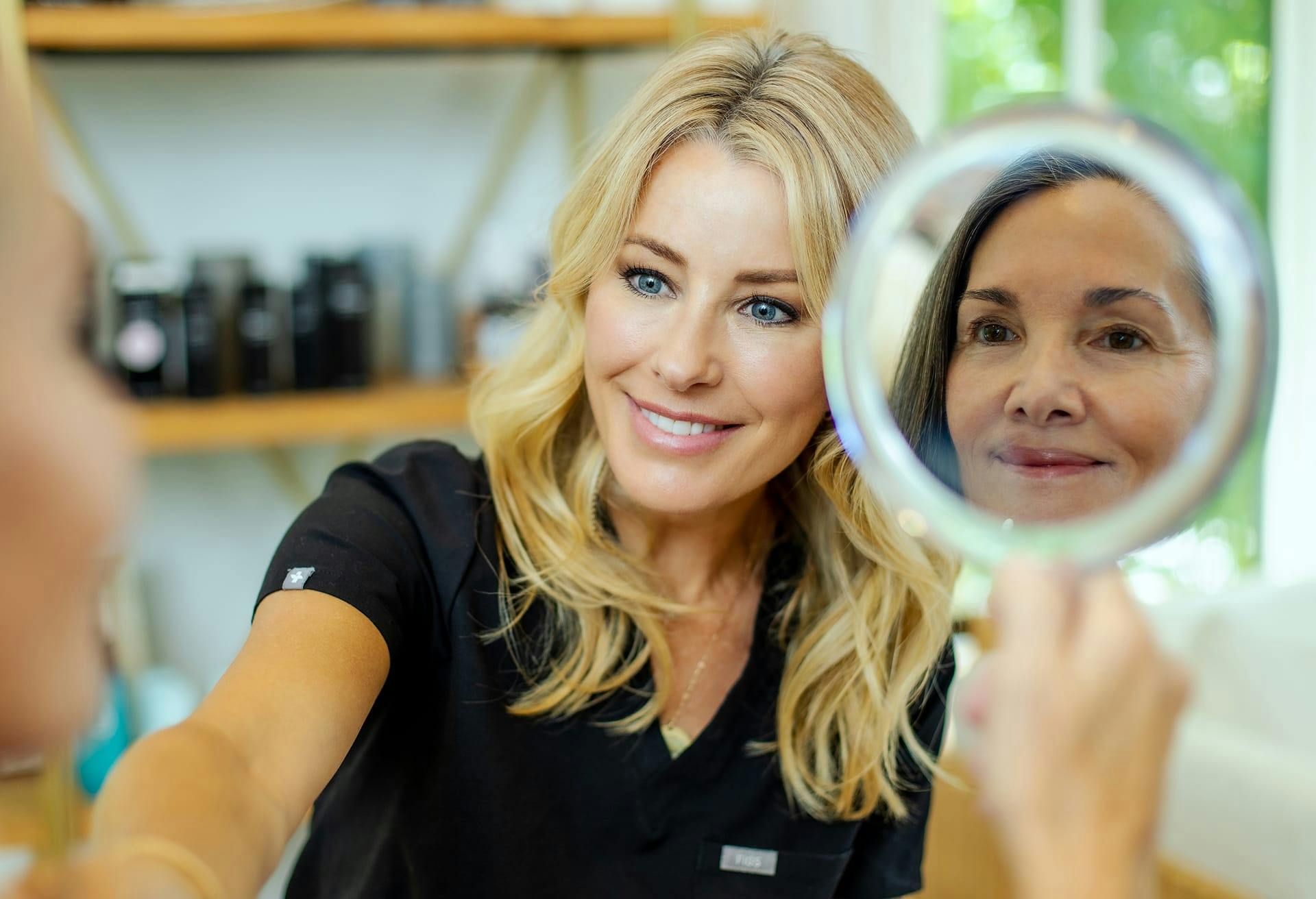 woman smiling while looking at client as she looks into handheld mirror
