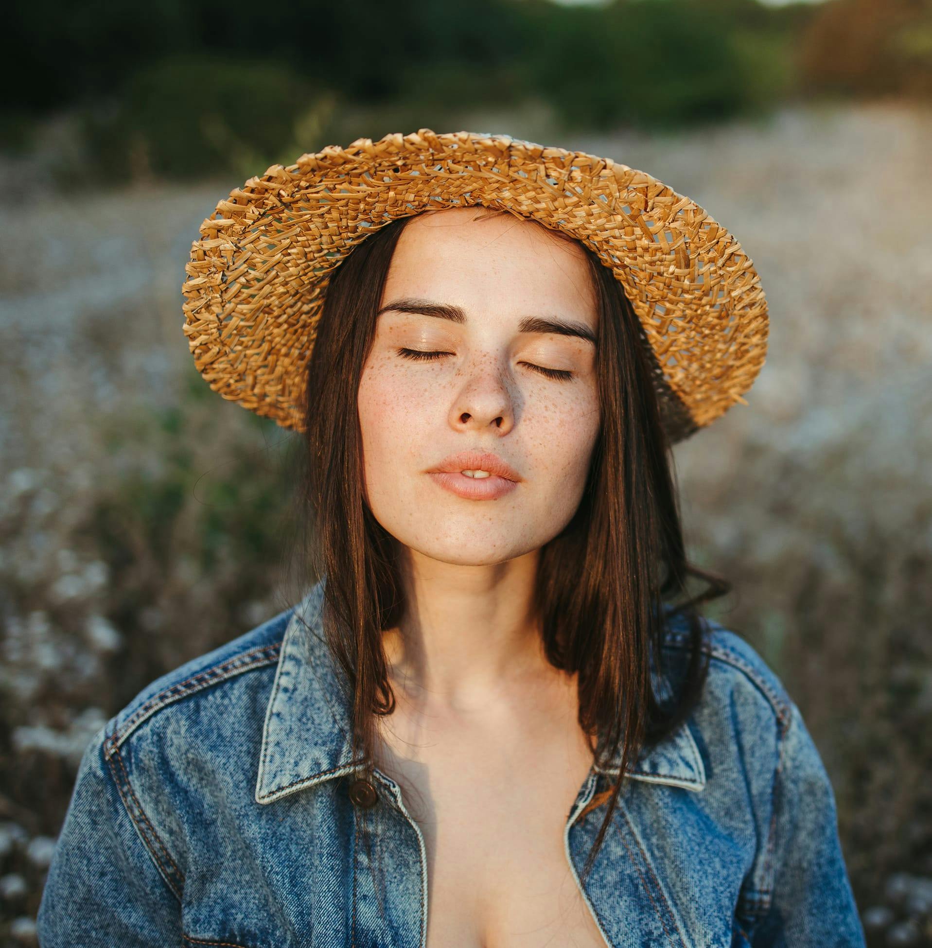 woman closing her eyes with hat on and jean jacket