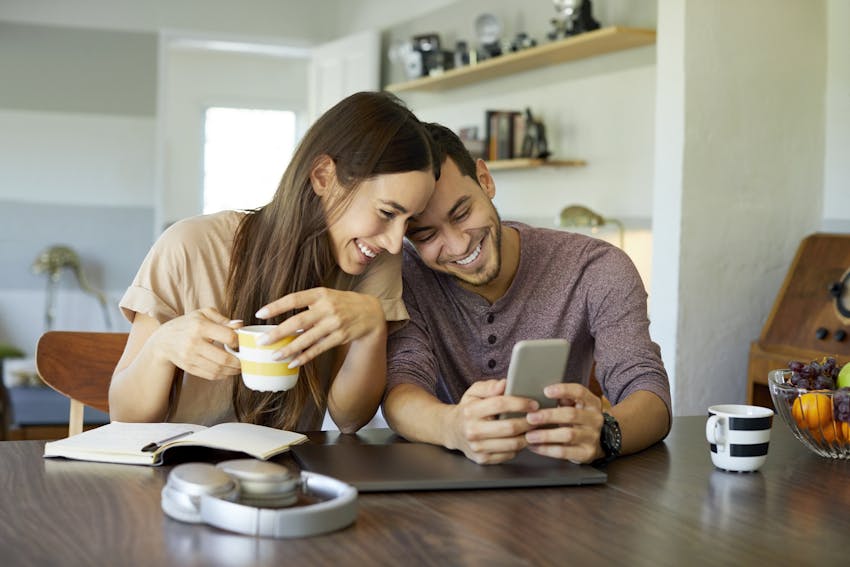 couple smiling while drinking coffee and looking at a phone