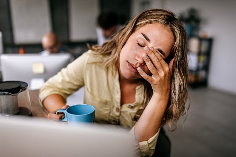 Tired and exhausted young female entrepreneur drinking coffee