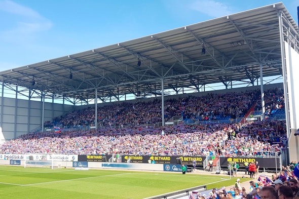 Tribune NÜSSLI pleine à craquer pour le match de football de Holstein Kiel sous un ciel bleu.