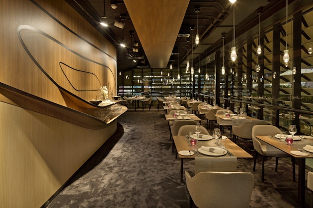 Elegantní interiér restaurace v německém pavilonu na Expo Milano 2015 se zakřivenou dřevěnou stěnou a položenými stoly.