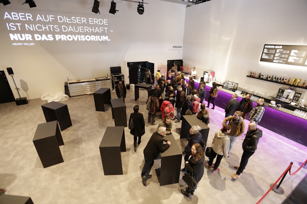 Besucher im Foyer des temporären Theater-Kubus Bern mit Kubus-Bar und Henry-Miller-Zitat