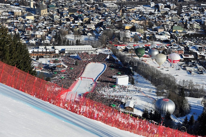 Zona de meta de la carrera del Hahnenkamm en Kitzbühel, con las gradas repletas, globos aerostáticos y vistas panorámicas de la ciudad
