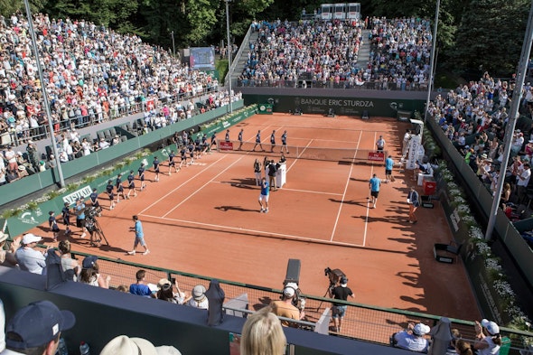Tribunas repletas en el ATP 250 Geneva Open, disputado en pista de tierra batida; los jugadores hacen su entrada al campo bajo el patrocinio de la Banque Eric Sturdza