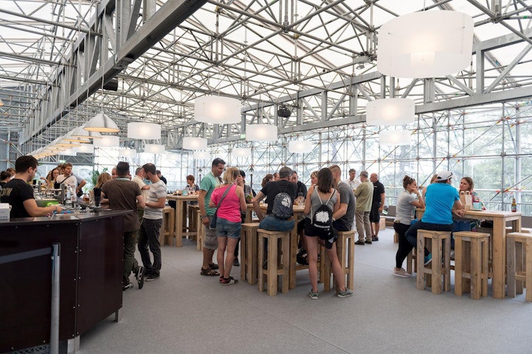 Tenda di ospitalità vivace con tavoli da bar in legno al Gurtenfestival 2017, costruzione in acciaio con facciata in vetro.