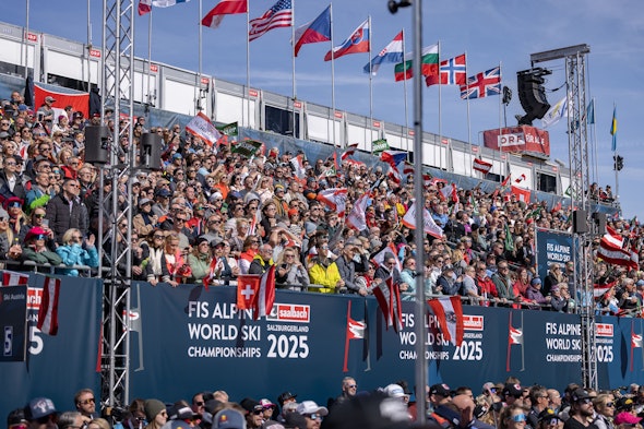The packed NÜSSLI grandstand, adorned with international flags, at the 2025 FIS Alpine World Ski Championships in Saalbach.