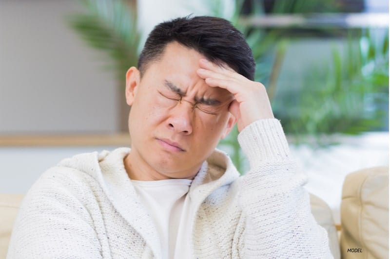 A young man with a headache holding forehead.