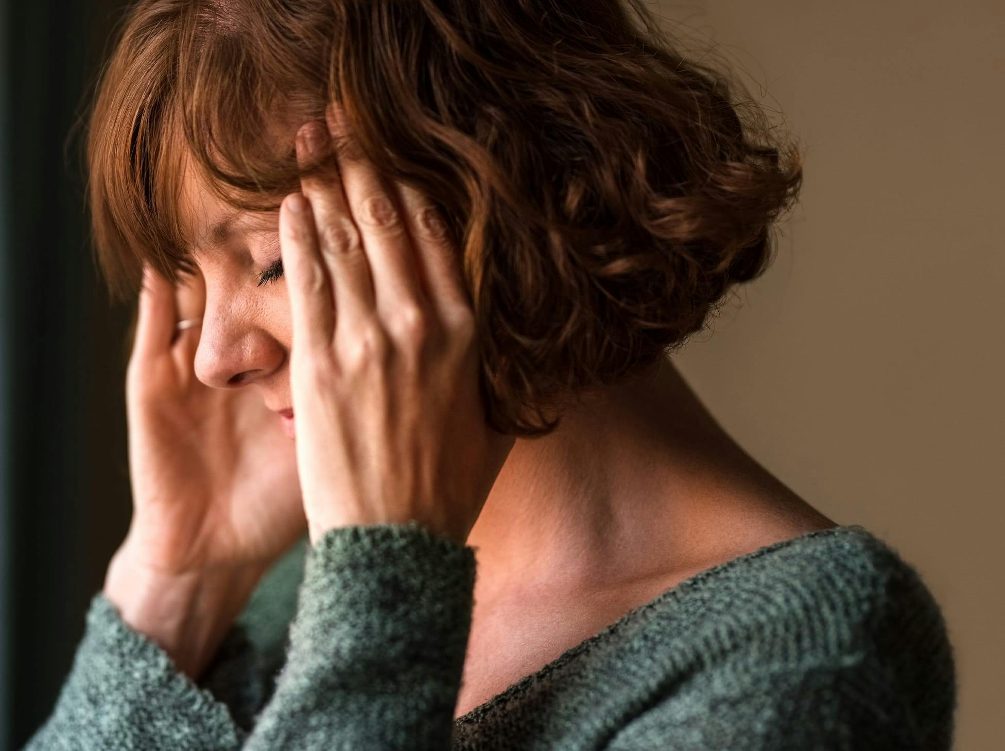 woman holding her temples, closing her eyes in pain