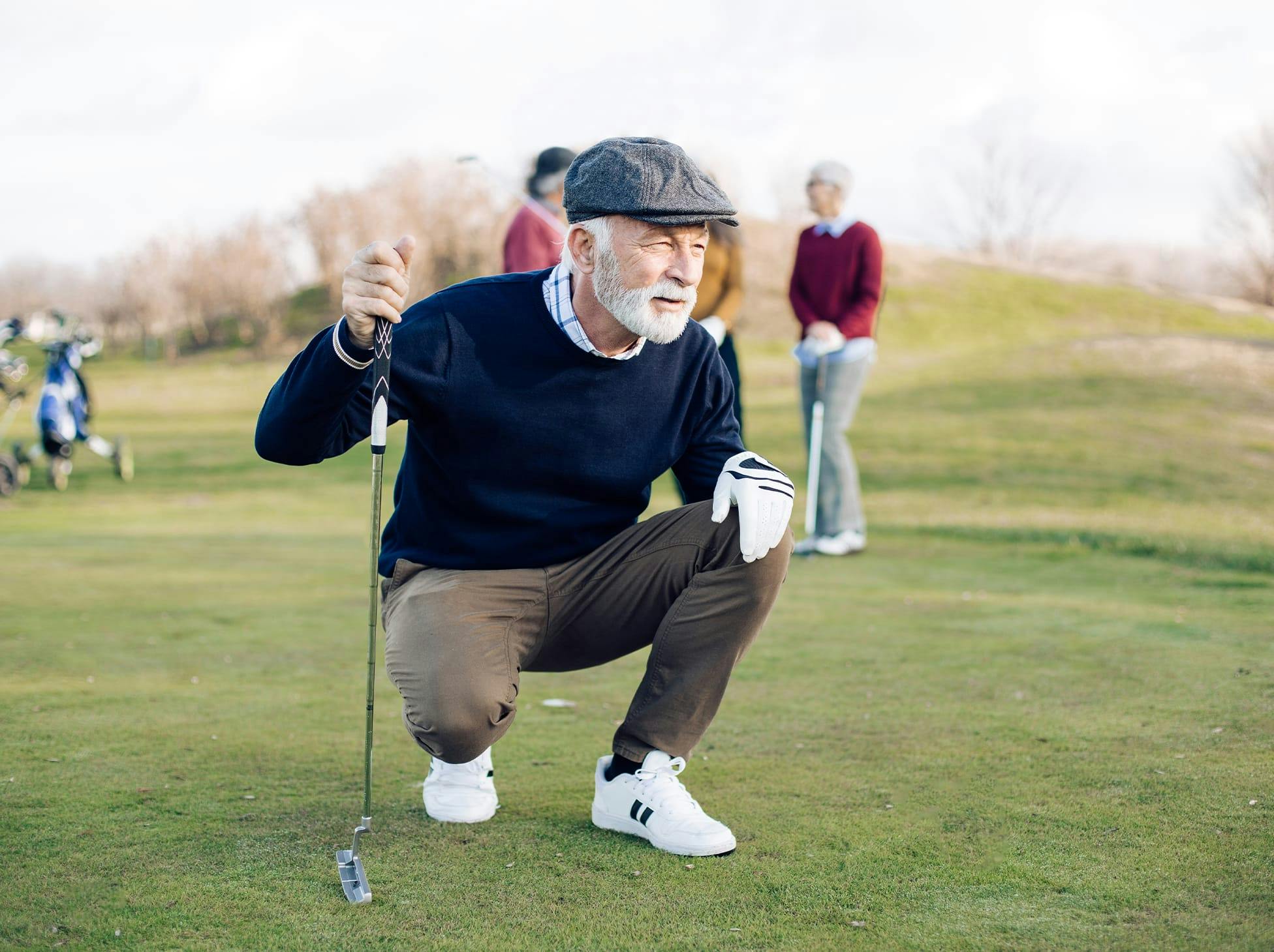 older man kneeling down on a gold course, holding a golf club